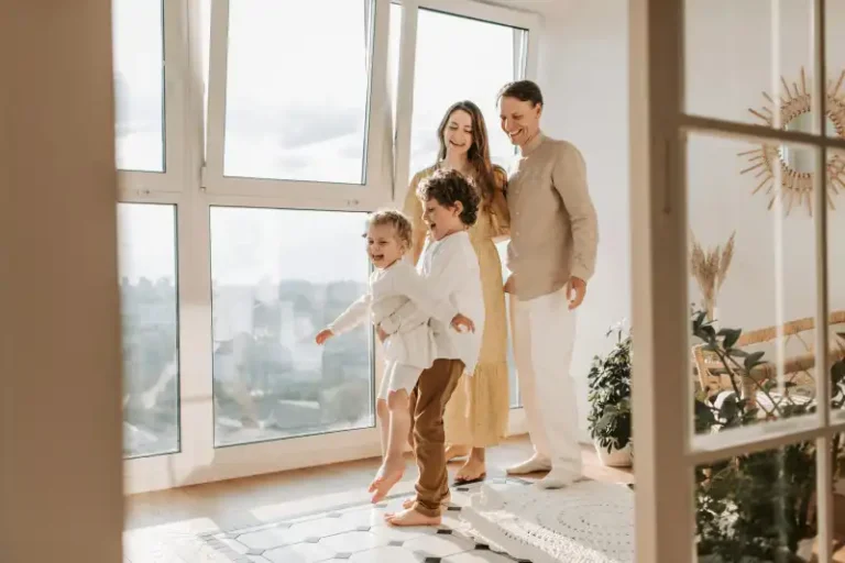 A family of four stands together by a large window